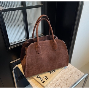 Detalle de bolso tote de ante marrón oscuro con textura mate y asa de mano doble