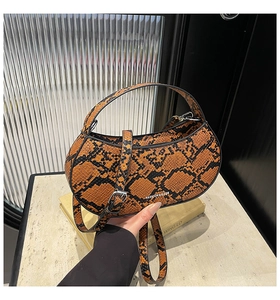 Detail of crescent snake-pattern handbag with silver FASHION & BAGS logo and strap