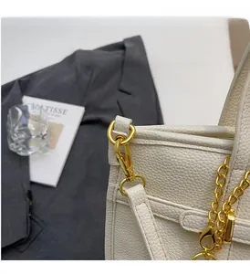Detail of white lychee leather handbag featuring elegant gold hardware and decorative chain