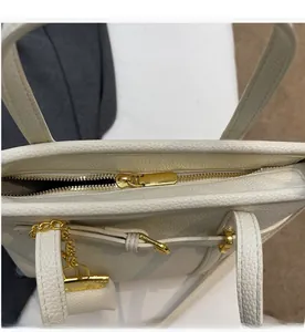 Detailed top view of a white lychee leather handbag featuring a smooth gold zipper closure