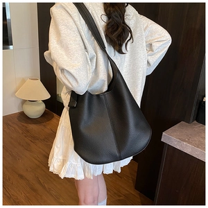 Rear view of model wearing a black litchi grain leather hobo bag with wide shoulder strap