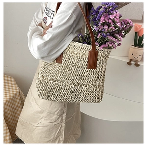 Detail of a beige woven straw tote bag with brown leather handles and interior floral decor