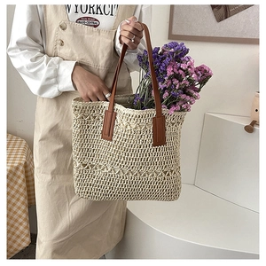 Detailed close-up of woven straw tote bag with brown leather handles and hollow crochet pattern