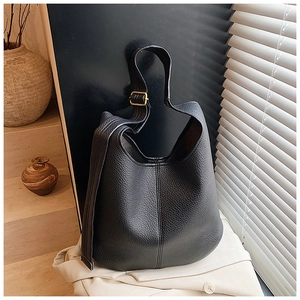 Detailed close-up of a black lychee pattern leather bucket bag with gold metal buckle