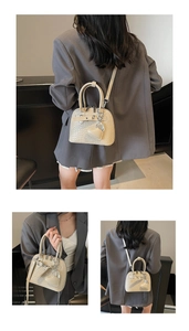 Close-up of beige woven texture shell bag with heart charm and slim strap