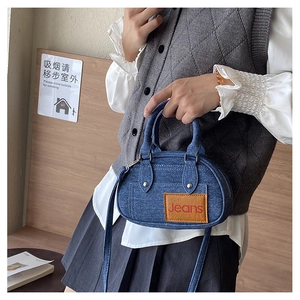 Detailed close-up of dark blue denim handbag with brown leather logo patch and dual handles
