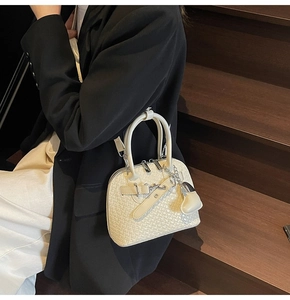 Detailed view of woven texture on a cream white shell bag with elegant chain ornament