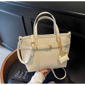 Detail of lychee textured cream tote bag with gold buckle and mini decorative charm