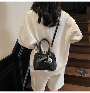 Detail view of a black woven shell bag with heart charm and shoulder strap