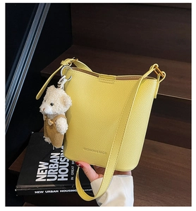 Detail of yellow litchi pattern bucket bag with a cute teddy bear plush charm and gold buckle