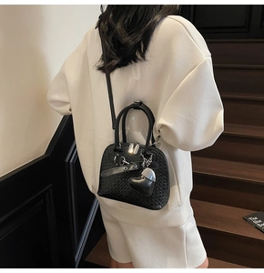 Detail of black woven shell bag with silver heart charm on model in staircase setting