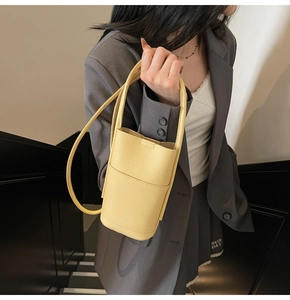Pale yellow lychee pattern leather bucket bag shown on a model in a casual business setting