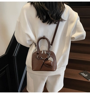 Close-up of dark brown shell bag with woven texture and heart charm worn by model