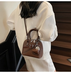Detail view of woven leather shell bag in dark brown with heart charm and crossbody strap