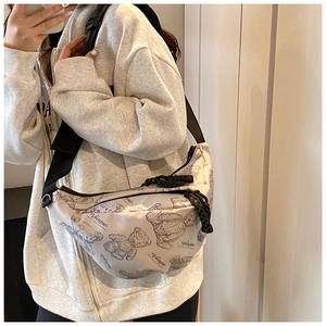 Detail der cremeweißen Umhängetasche mit Bärenprint und schwarzem Gurt am Model