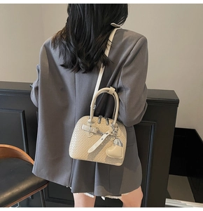 Detail of beige woven texture shell bag worn with a grey blazer for a chic look