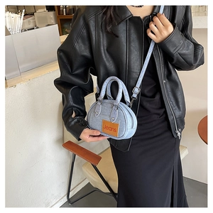 Close-up of light blue denim handbag with brown leather patch and crossbody strap