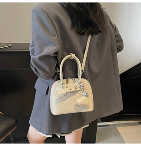 Detail of off-white crocodile embossed crossbody bag with heart pendant on gray coat