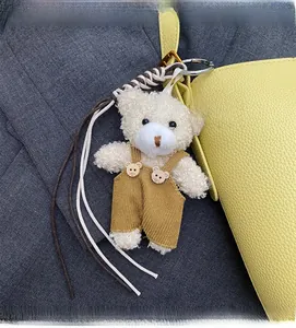 Detail of cute cream plush teddy bear charm with corduroy overalls on yellow bucket bag