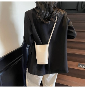 Detail view of off-white lychee grain leather mini crossbody bag on model with black suit