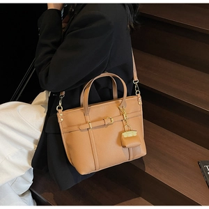 Detail view of brown lychee grain leather handbag with gold buckle and mini bag charm