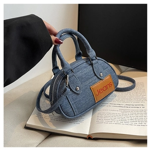 Detail of blue denim mini bowling bag featuring brown leather Jeans label and silver studs