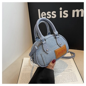 Detail view of denim handbag with brown leather jeans patch and metal zipper close-up