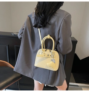 Detail of yellow woven texture mini shell bag with a cute heart charm on crossbody strap