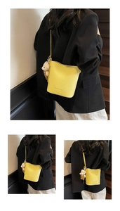 Detail view of yellow lychee texture bucket bag with plush bear charm and long strap