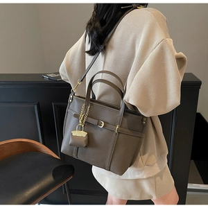 Detail of lychee pattern leather tote bag with gold buckle and mini charm accessory