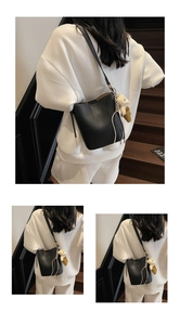 Detail of black litchi grain bucket bag with a beige plush bear charm decoration