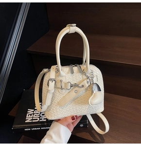 Close-up of cream woven texture shell bag with silver buckle and heart charm on wood stairs