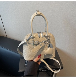 Detail of cream woven texture PU shell bag with silver heart charm on black books
