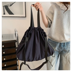 Detalle de un bolso hobo negro grande con cierre de cordón y correa ancha ajustable