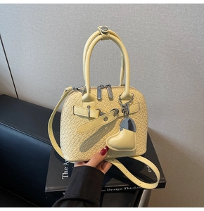 Close-up of pale yellow woven texture shell bag with heart-shaped charm detail
