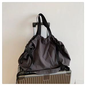 Detalle de bolso tote gris oscuro con cordón sobre maleta plateada para viajes y oficina