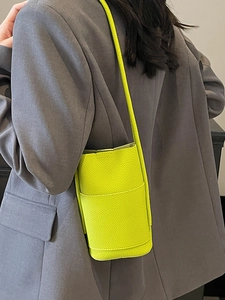 Minimalist litchi textured neon green cylinder crossbody bag shown on a suit shoulder