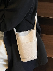 Minimalist white lychee grain PU leather bucket crossbody bag worn by model over black suit
