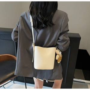 Detail view of cream lychee texture bucket bag with adjustable strap and bear pendant
