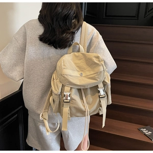 Beige nylon backpack with drawstring closure and silver metal buckles on wooden stairs