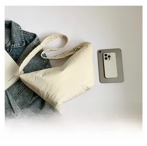 Detail of cream pleated shoulder bag shown with a phone and book for size comparison