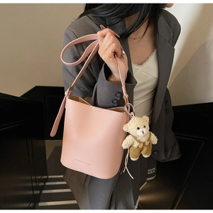 Pink lychee grain bucket bag with cute bear charm worn by a model in casual grey suit