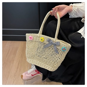 Detail of hand-woven straw tote bag with colorful 3D fabric flowers and a gingham bow tie