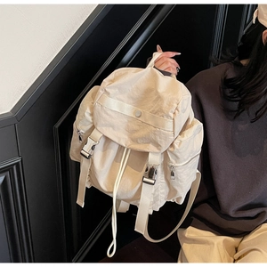 Detail shot of cream-colored nylon backpack showing buckle closures and side zip pocket