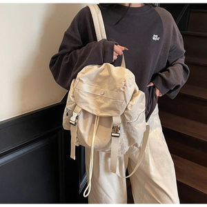 Detail view of cream nylon backpack featuring plastic buckle closure and multi-pocket structure