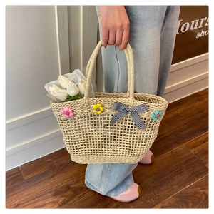 Detail of straw woven tote bag featuring colorful plush flowers and checkered bow decoration