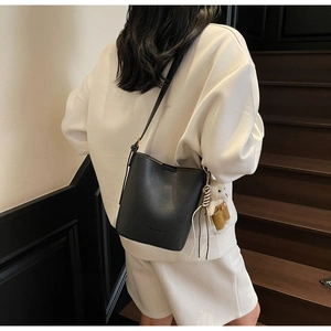 Detail of black lychee leather bucket bag with a cute white bear plush pendant
