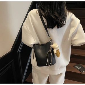 Detail of black litchi pattern bucket bag with cute bear charm worn on white hoodie