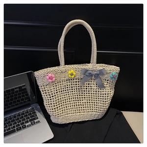 Close-up of beige woven straw tote bag with 3D floral accents and checkered bow tie