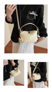 Detail of cream crescent saddle bag with metal turn-lock and pearl charm pendant